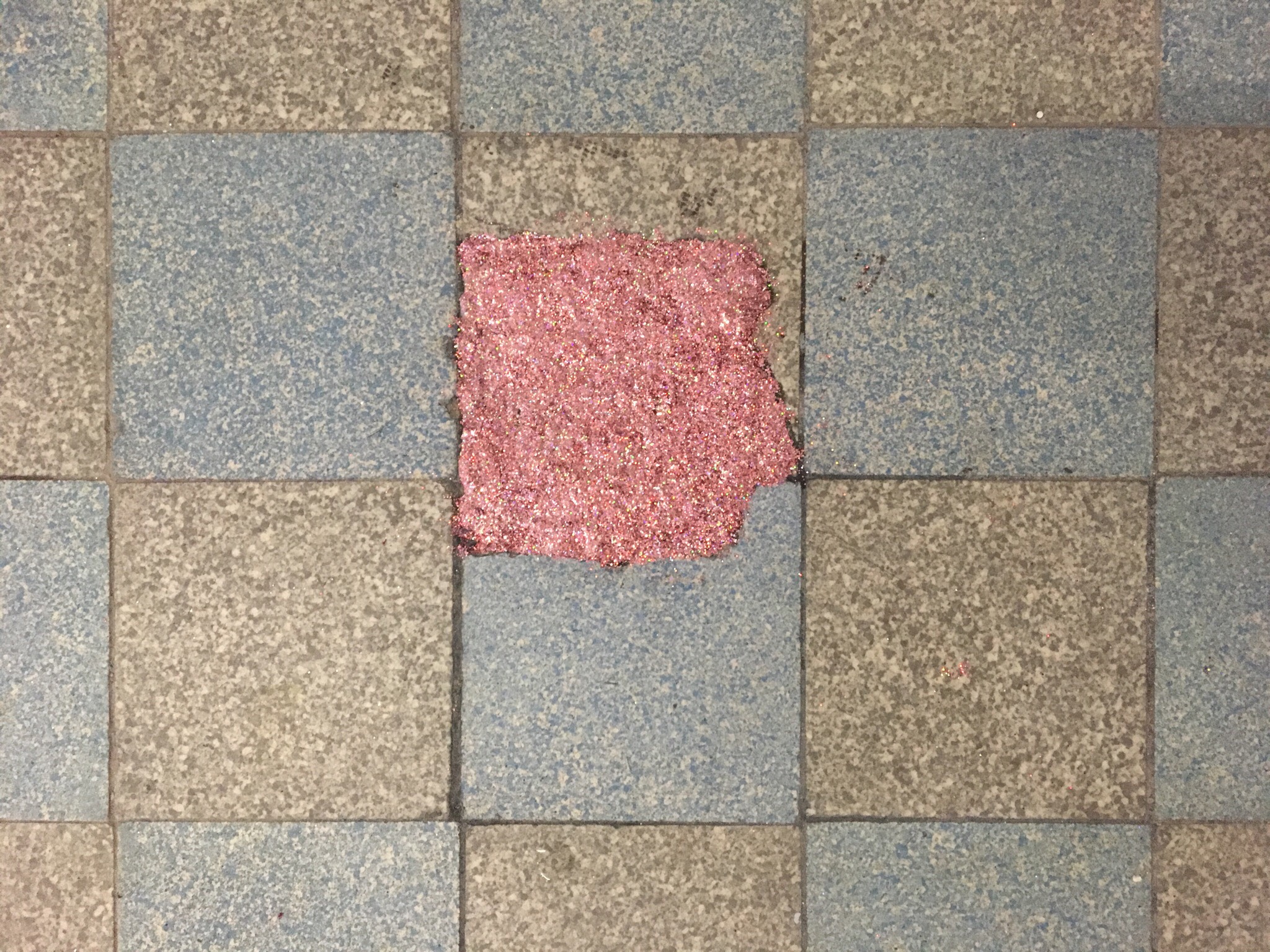 Un sol de carrelage est abimé, il semble manquer un carreau. Il a été réparé avec un applat de paillettes roses.